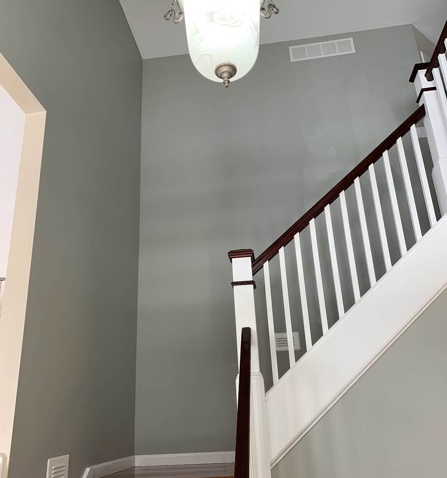 A two-story stairwell painted gray, with a white staircase, stained handrail, a frosted glass pendant light and a wood-floored landing.